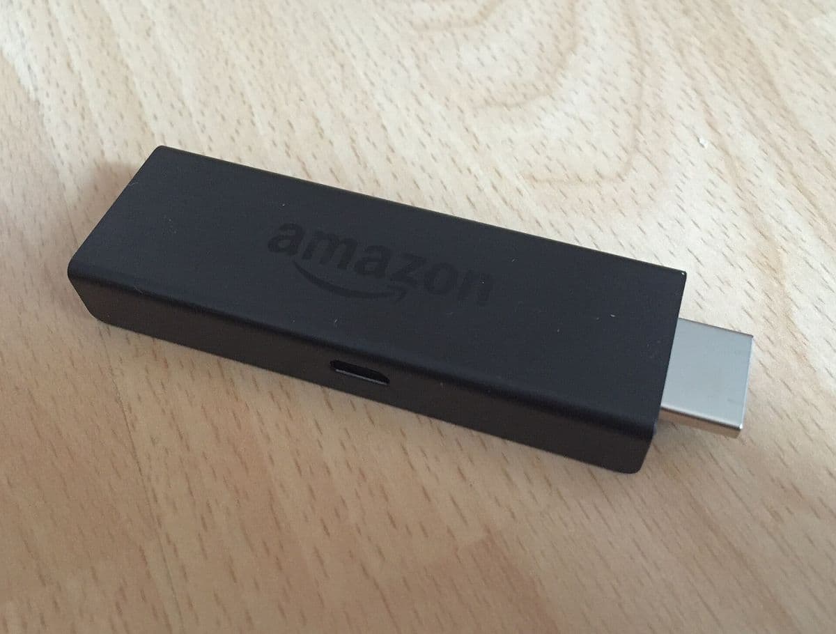 Black Amazon Fire TV Stick with its HDMI connector, on a wooden table